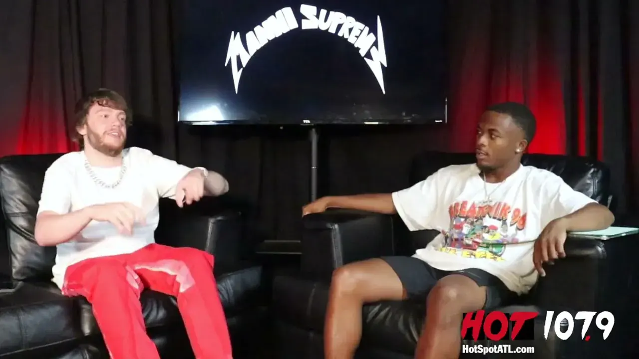 Murda Beatz and an interviewer on a leather couch in a radio studio beside the Hot 107.9 logo