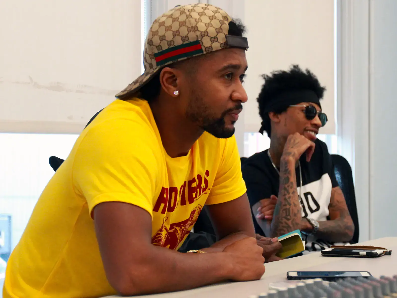 Two producers at a panel table, one in a yellow shirt and patterned cap, the other in sunglasses