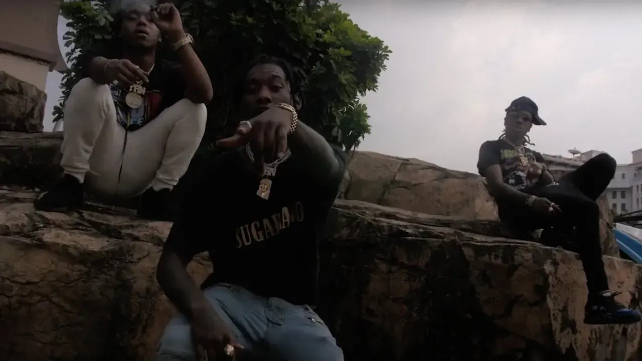 The three members of Migos sit outside on stone steps and a low wall