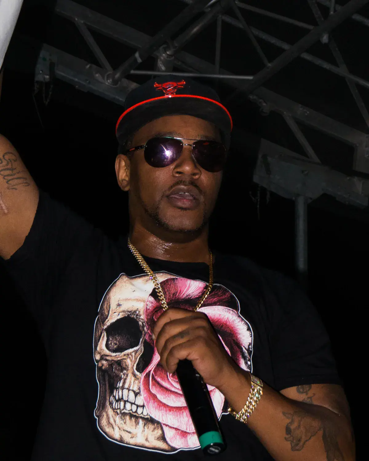 Cam’ron in sunglasses and a cap raps into a microphone with one arm raised
