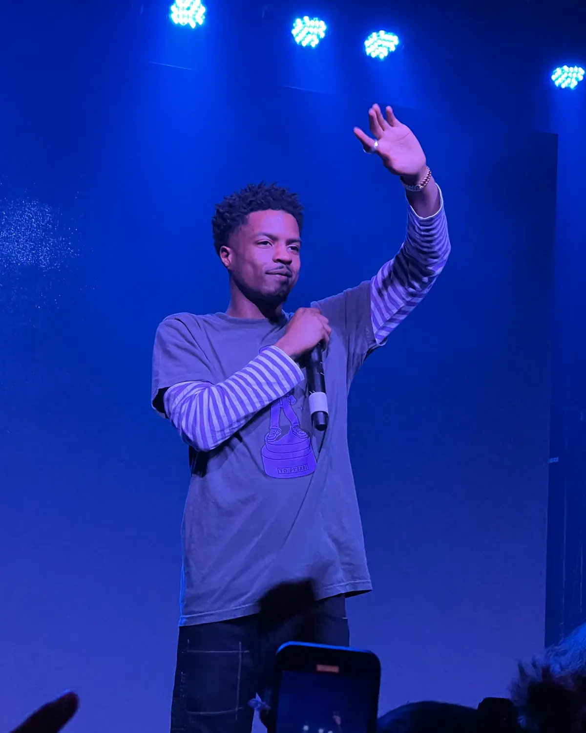 Pi’erre Bourne on a blue-lit stage holding a microphone with one hand raised